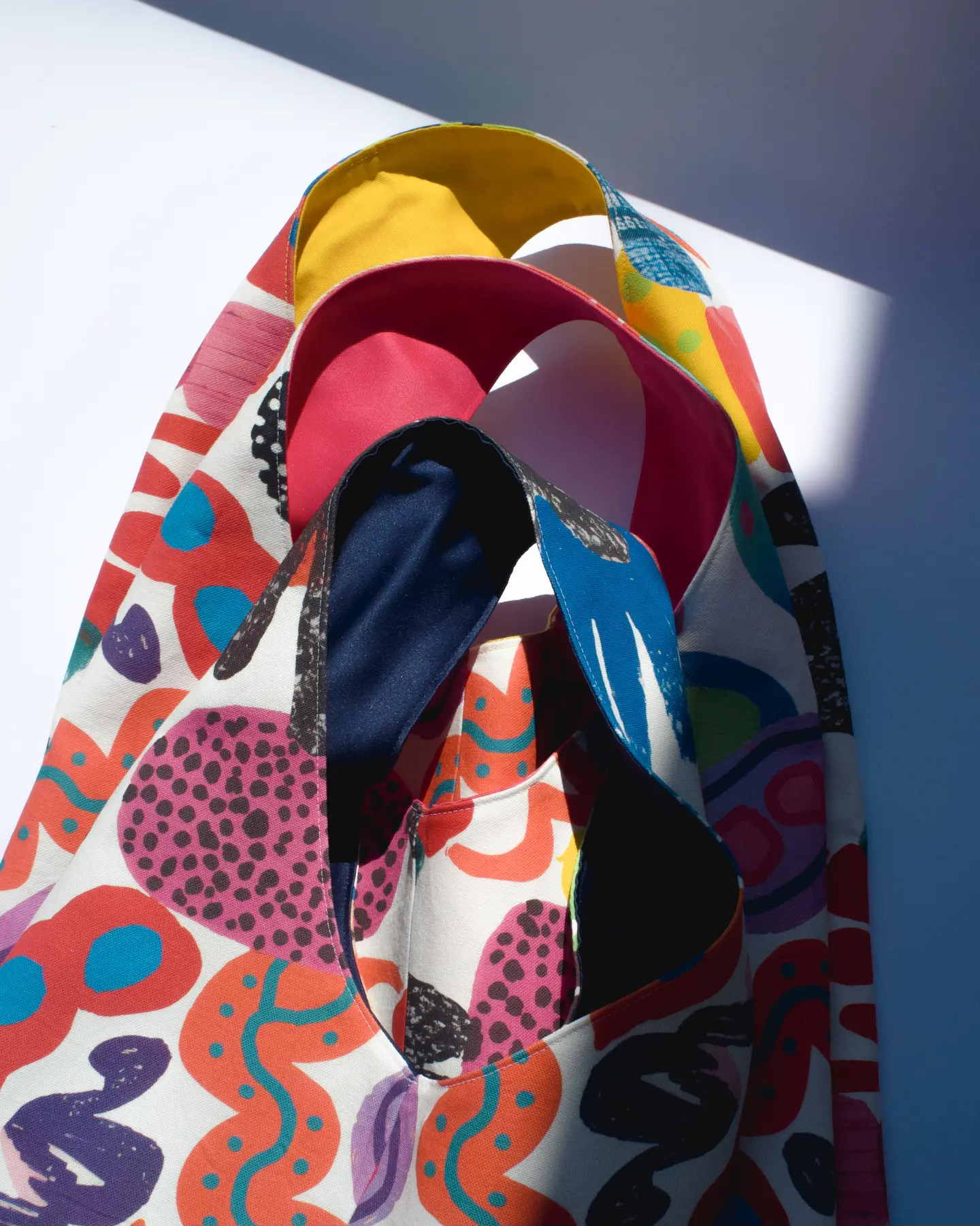 Nekoliko platnenih torbi sa apstraktnom štampom, složenih jedna preko druge u oštrom svjetlu