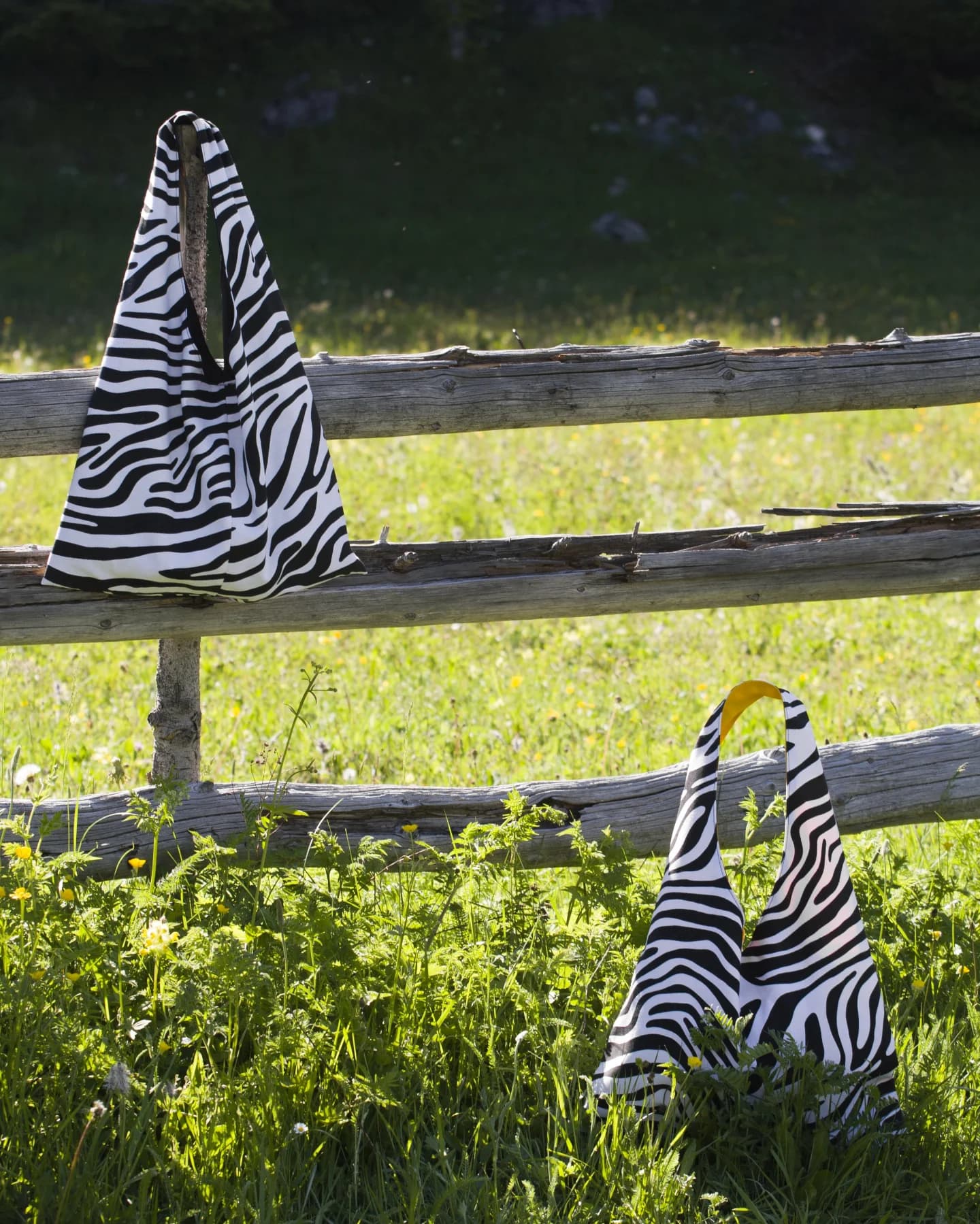 Dvije zebra torbe obješene o drvenu ogradu iznad planinske livade u cvatu